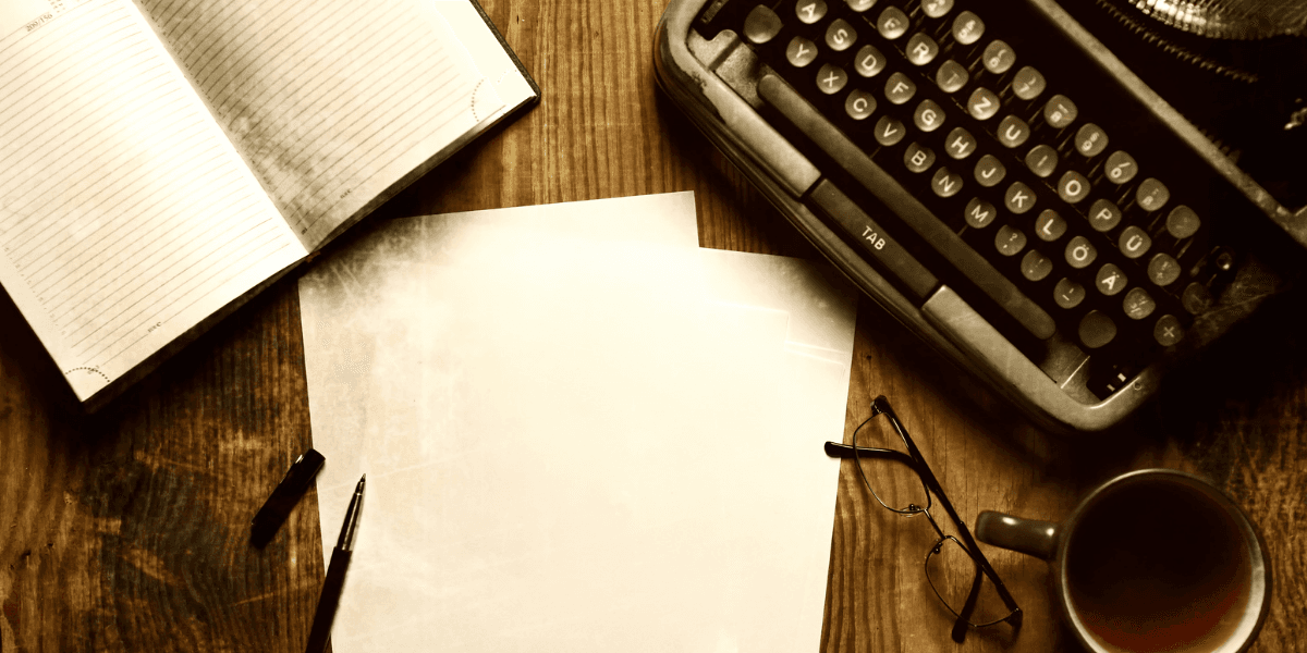 Typewriter, blank paper, notebook, pen, glasses, and coffee cup on wooden table