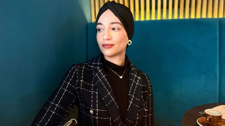 Author Amina Abaira wearing a decorative black headscarf in a close-up portrait.