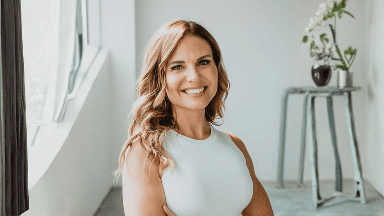 Angela Porrelli smiling in a white sleeveless top in a bright modern interior.