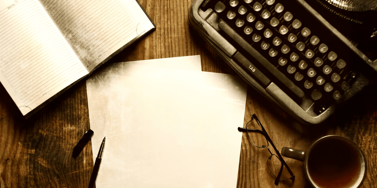 Typewriter, blank paper, notebook, pen, glasses, and coffee cup on wooden table