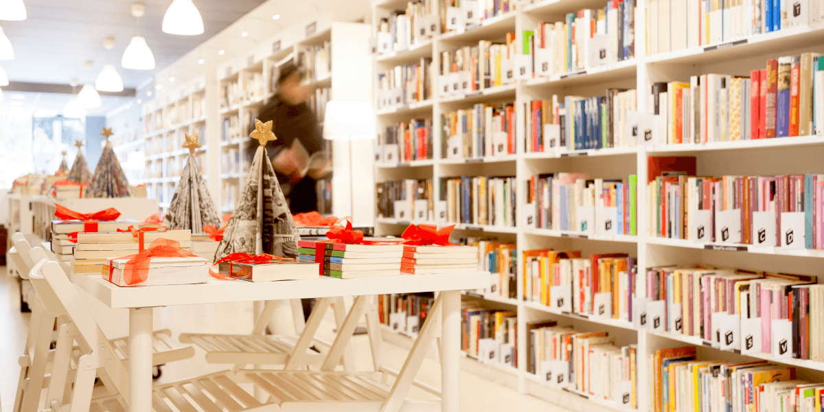 A bright library with bookshelves, tables decorated for the holidays, and a person browsing.