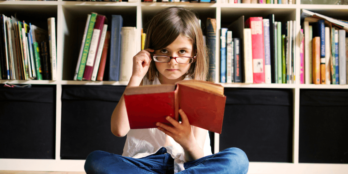 Young girl sitting on the floor reading a book in front of a bookshelf