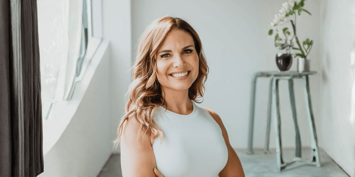 Angela Porrelli smiling in a white sleeveless top in a bright modern interior.