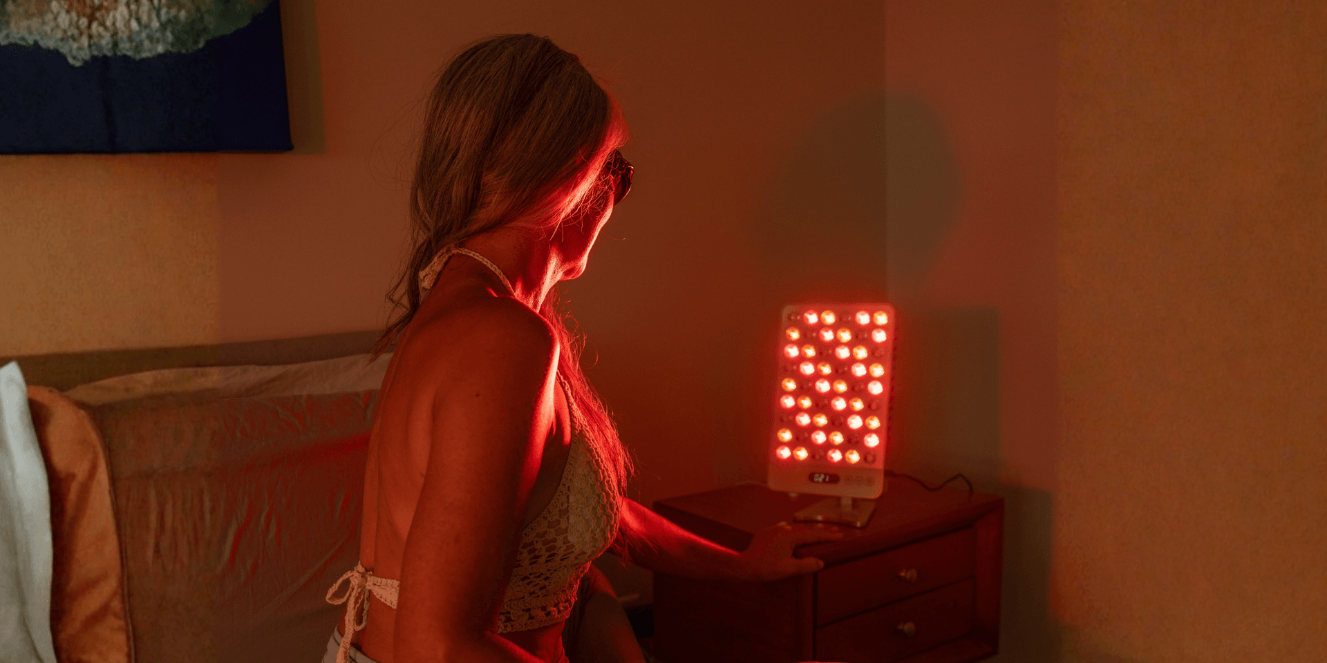 Woman in a swimsuit using a red light therapy device in a bedroom setting