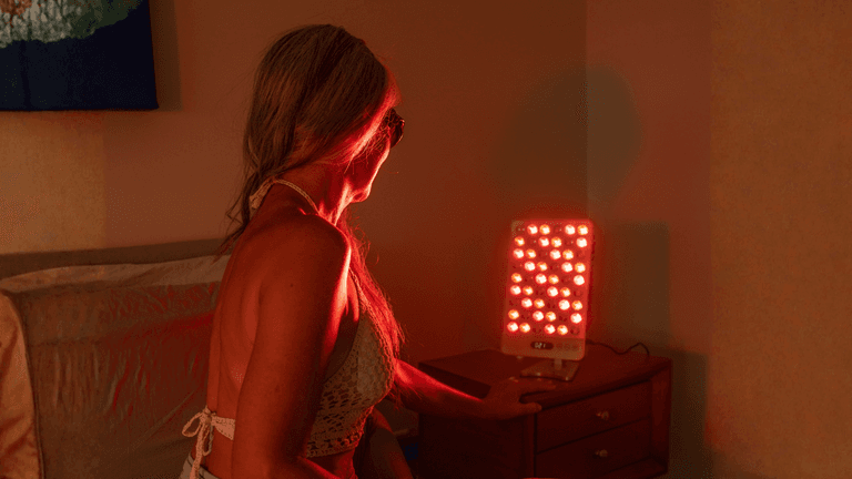 Woman in a swimsuit using a red light therapy device in a bedroom setting