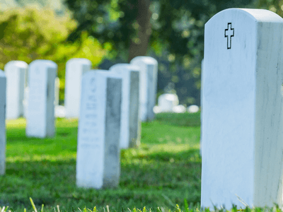 White gravestones in a cemetery, with a grassy landscape and trees in the background