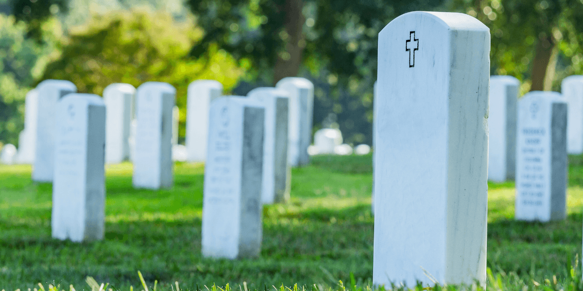 White gravestones in a cemetery, with a grassy landscape and trees in the background