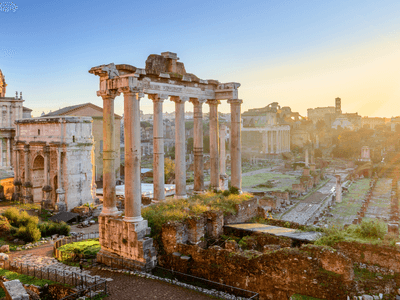 Sunrise over ancient Roman ruins with columns and historical buildings in the background