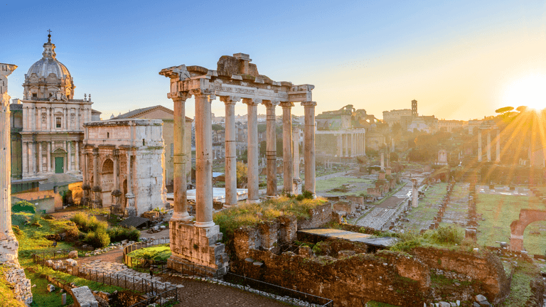 Sunrise over ancient Roman ruins with columns and historical buildings in the background