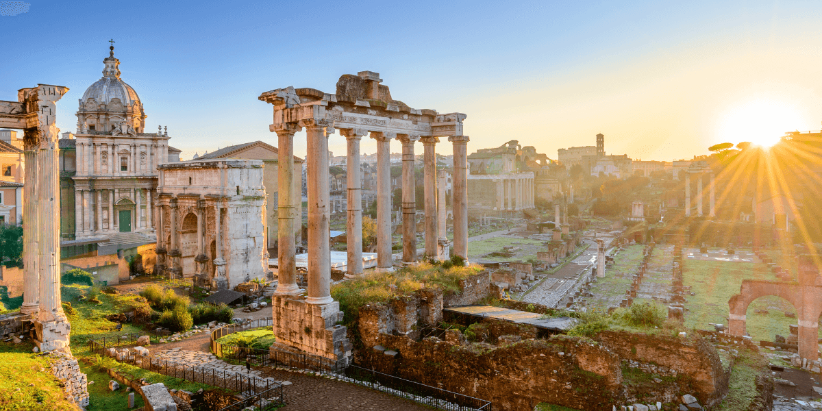 Sunrise over ancient Roman ruins with columns and historical buildings in the background