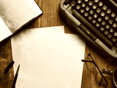 Typewriter, blank paper, notebook, pen, glasses, and coffee cup on wooden table