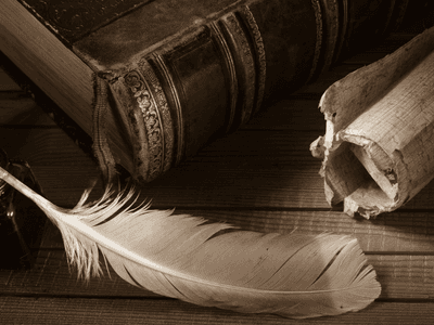 Antique book, feather quill, ink bottle, and rolled parchment on a wooden table