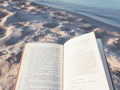 Open book resting on sandy beach near water's edge
