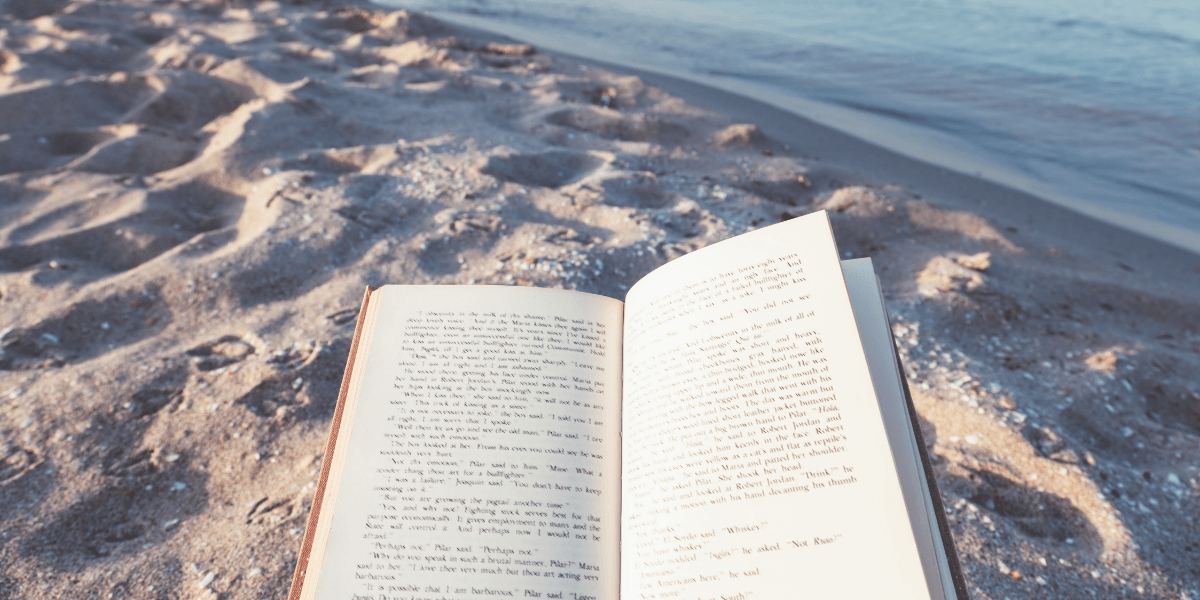 Open book resting on sandy beach near water's edge