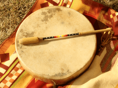 A round drum with a beater resting on a colorful woven blanket
