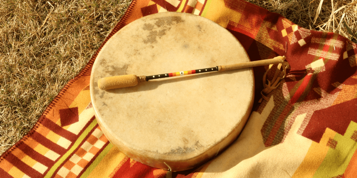 A round drum with a beater resting on a colorful woven blanket