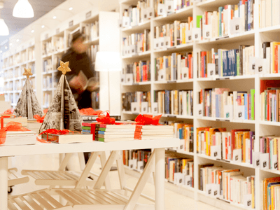 A bright library with bookshelves, tables decorated for the holidays, and a person browsing.