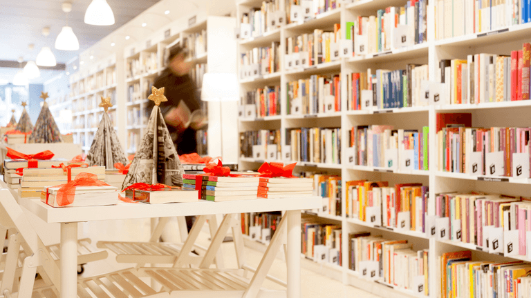 A bright library with bookshelves, tables decorated for the holidays, and a person browsing.