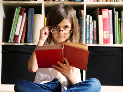 Young girl sitting on the floor reading a book in front of a bookshelf