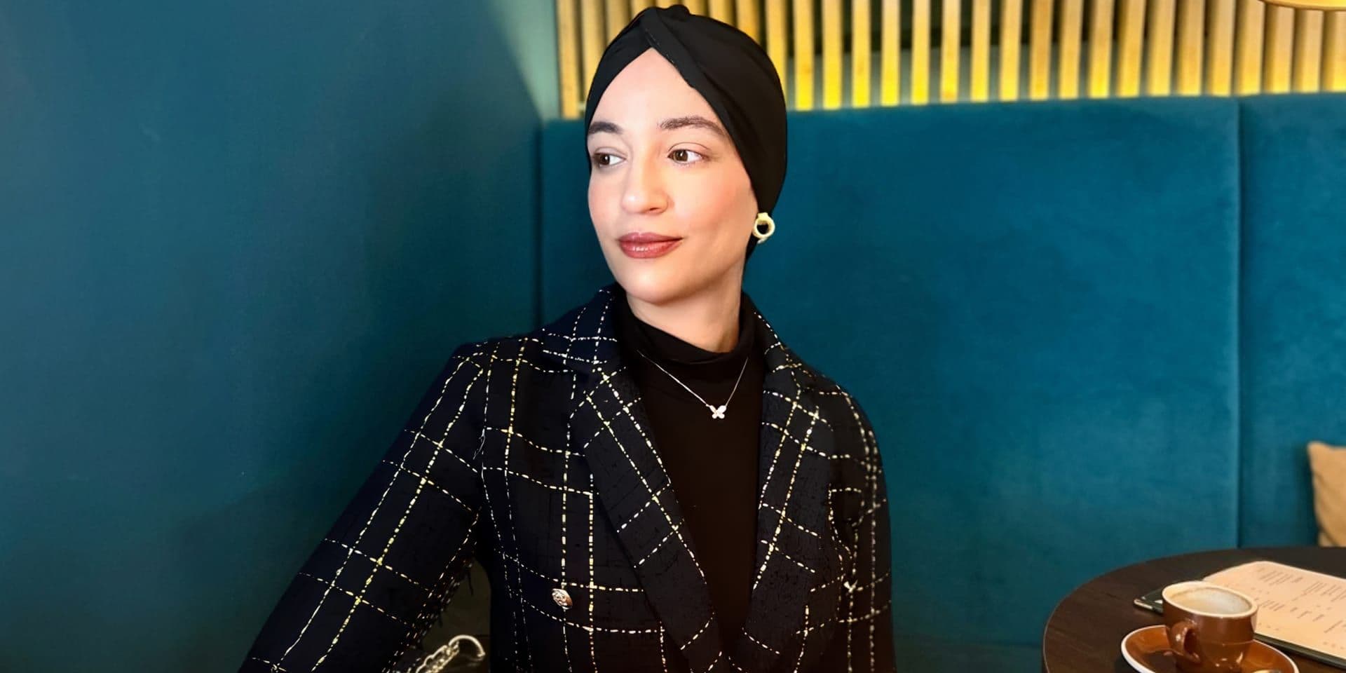 Author Amina Abaira wearing a decorative black headscarf in a close-up portrait.