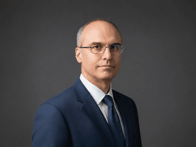 Alessandro Catorcini wearing a blue suit against a dark studio background.