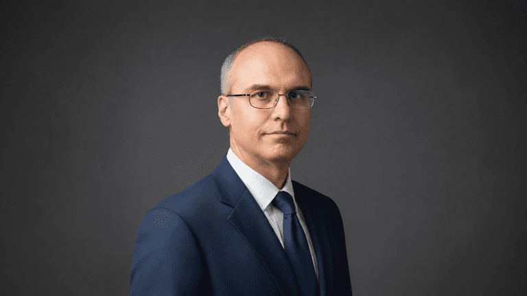 Alessandro Catorcini wearing a blue suit against a dark studio background.