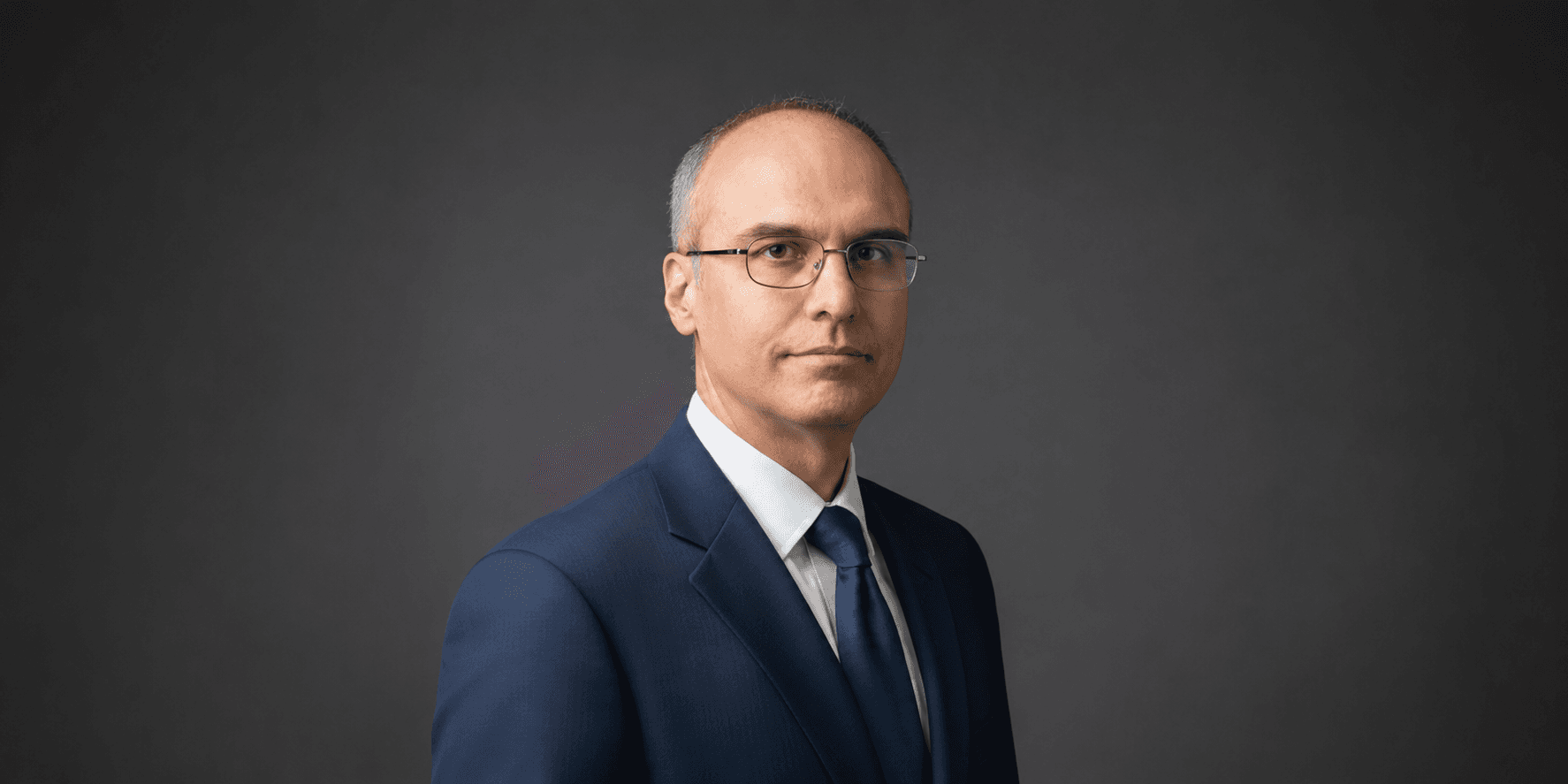Alessandro Catorcini wearing a blue suit against a dark studio background.