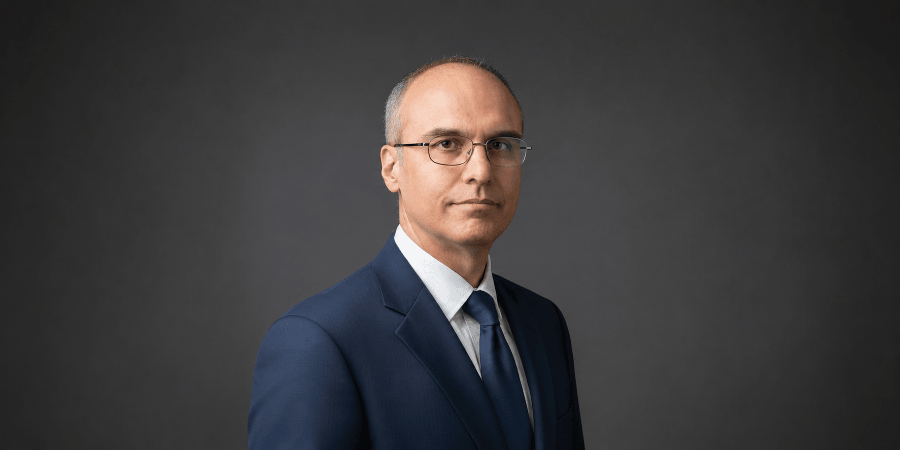Alessandro Catorcini wearing a blue suit against a dark studio background.